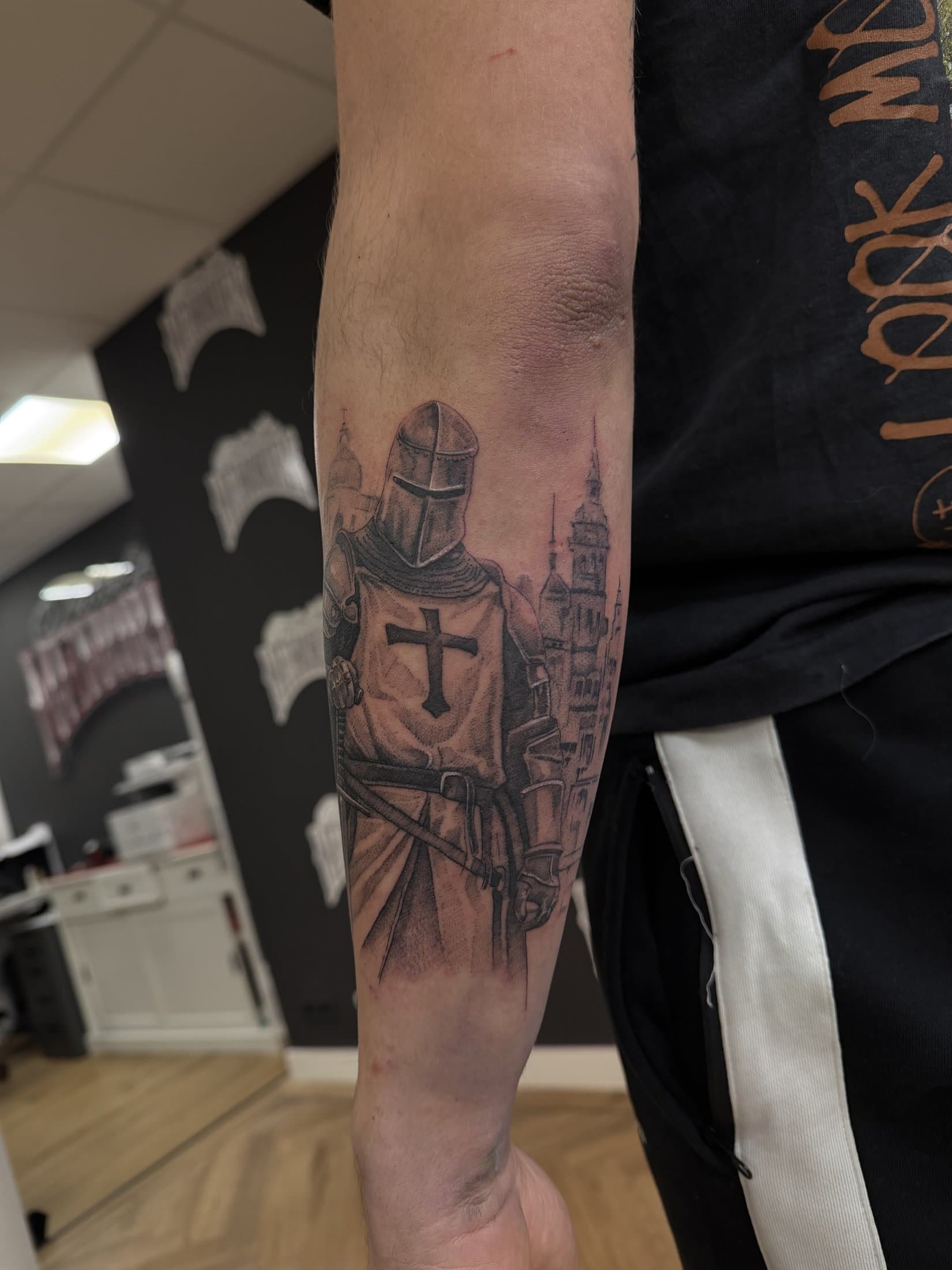 Templar knight with a cross shield in front of a medieval city, on the forearm